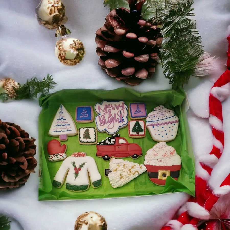 Box of Christmas sugar cookies with a Merry and Bright plaque, red truck, ugly sweater and Santa cupcake